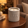 Graue Beton-Duftkerze Love mit Holzdocht und Feige-Cassis-Duft auf einem Holztisch im warmen Wohnzimmer