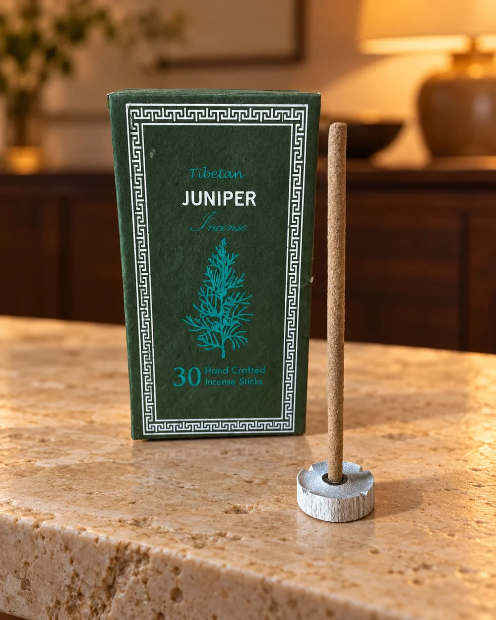 Dunkelgrüne Juniper-Box und ein unangezündetes Räucherstäbchen im Halter auf hellem Naturstein.