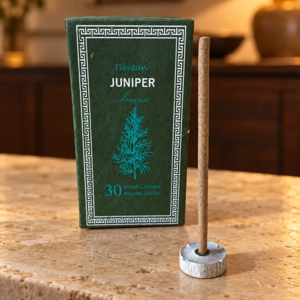 Dunkelgrüne Juniper-Box und ein unangezündetes Räucherstäbchen im Halter auf hellem Naturstein.